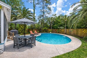 A backyard with a swimming pool, a covered patio with a table and chairs, and a wooden fence.