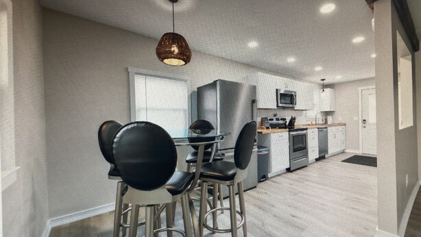 A modern kitchen with stainless steel appliances, a dining area with black chairs, and a hanging light fixture.