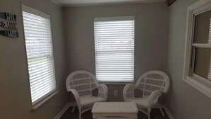 A room with two white chairs and a bench, a window with blinds, and a wall sign.