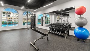 Un gimnasio con equipo de ejercicio, ventanas amplias y vistas a una piscina y edificios exteriores.