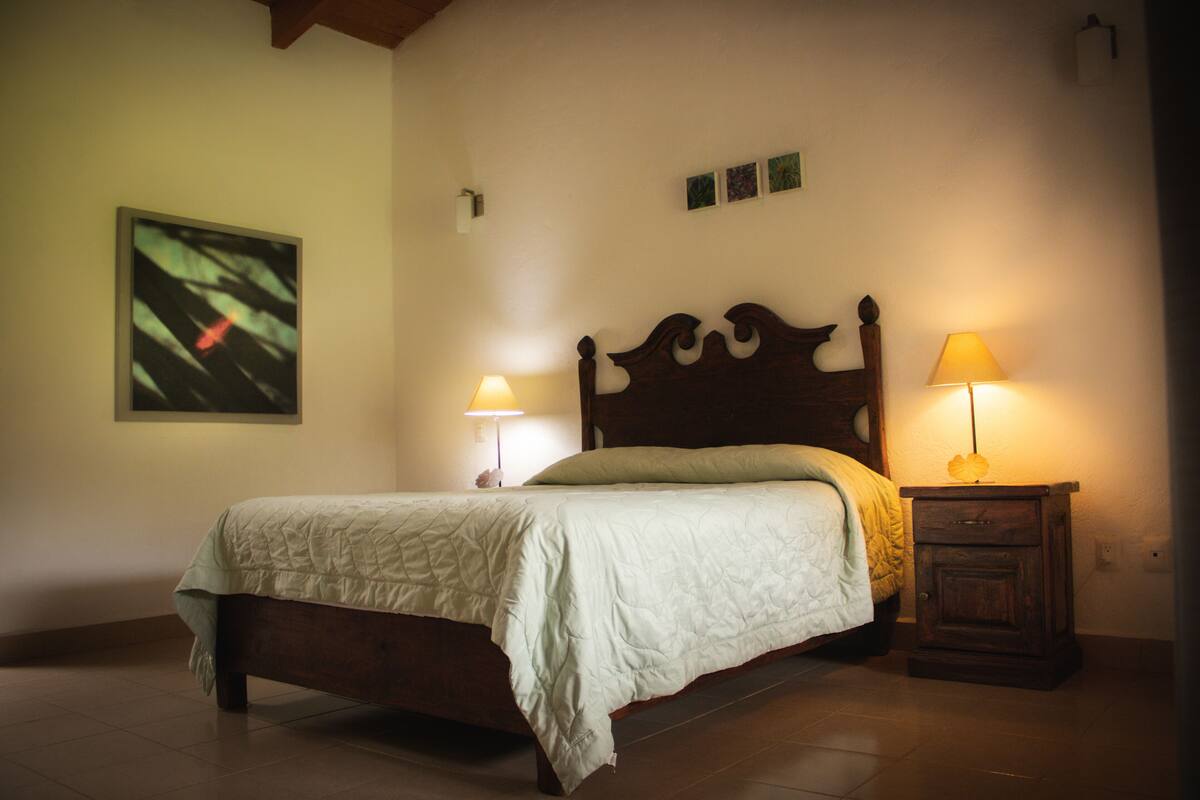 A bedroom with a wooden bed, two bedside lamps, a wall-mounted artwork, and a small cabinet.