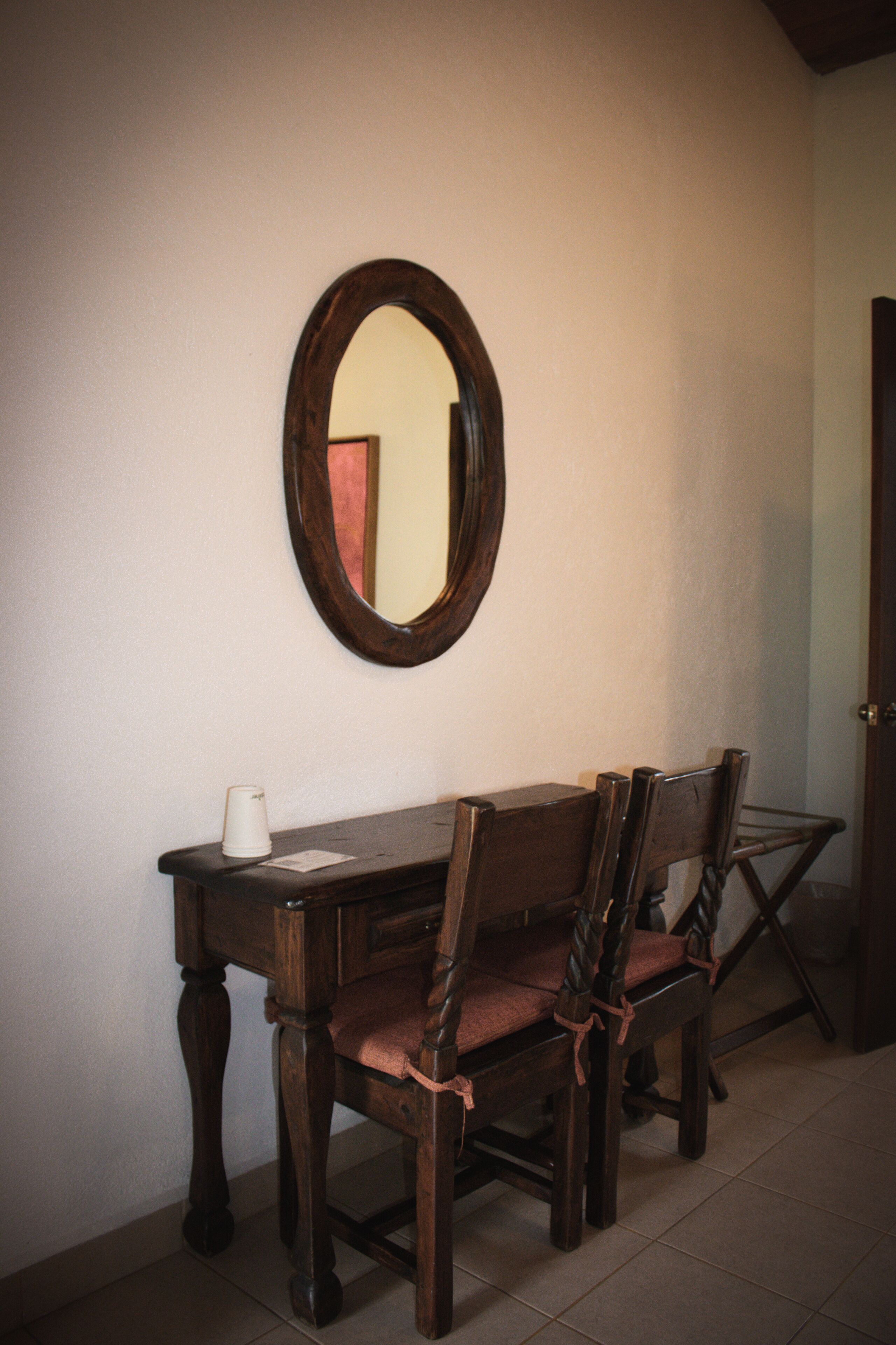 A dining area with a wooden table, two chairs, and a mirror on the wall.