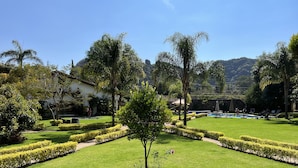 A well-maintained garden with manicured lawns, a swimming pool, and a clear view of a mountain in the background. - Hotel Posada La Presa (Tepoztlán)