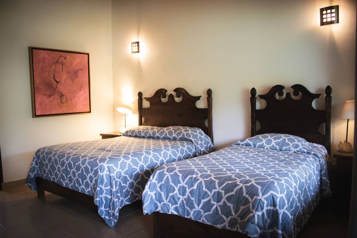 A room with two beds, each with a headboard and a bedside table.