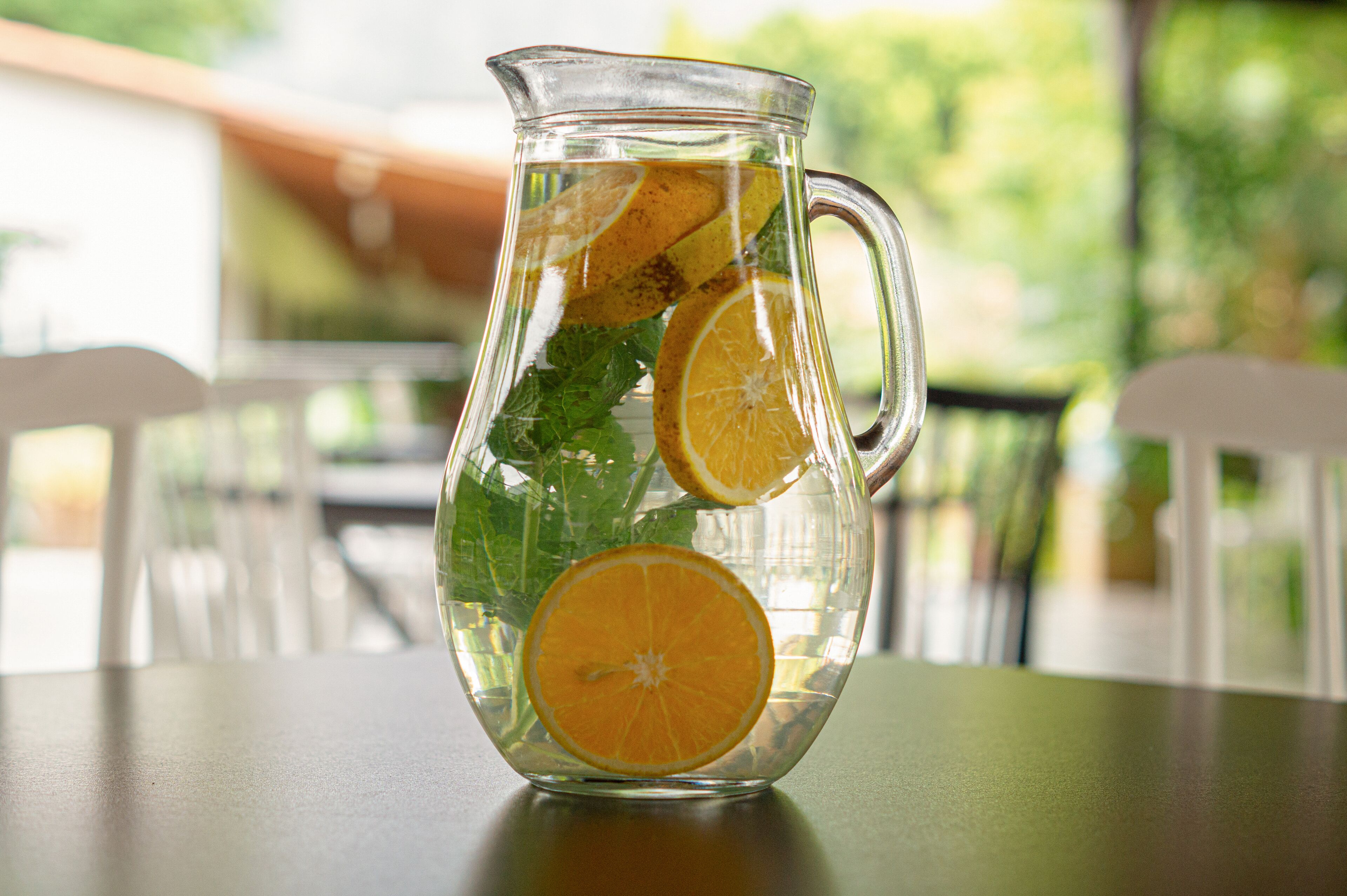 Une carafe en verre transparent, remplie d’eau, de feuilles de menthe et de tranches d’orange, est posée sur une table.