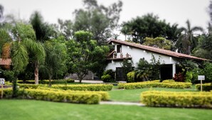 A white building with a red-tiled roof, surrounded by well-maintained hedges and trees. - Hotel Posada La Presa (Tepoztlán)