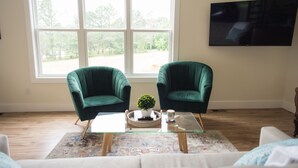 A living room with two green armchairs, a glass coffee table, a white sofa, and a large window with a view of trees. - "The Primm Loft" Private, Spacious, Clean & New (Murfreesboro)