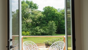 An open door leading to a balcony with two white chairs and a small table, overlooking a grassy area with trees. - "The Primm Loft" Private, Spacious, Clean & New (Murfreesboro)