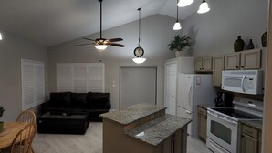 Un espacio habitable compacto con comedor, sofá, cocina equipada con microondas, horno y alacenas, y ventilador de techo.