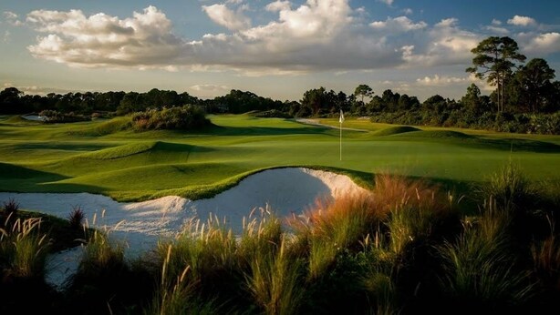 Un campo de golf con un estanque, árboles y cielo despejado.