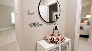 Una habitación con un espejo redondo en la pared, un adorno sobre una consola y una puerta que da a otra estancia.