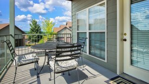 Eine überdachte Terrasse mit Tisch und Stühlen, eine Tür mit Fenster und Blick auf benachbarte Häuser.