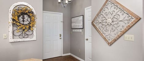 Un pasillo con una puerta blanca, una araña y detalles decorativos en la pared.