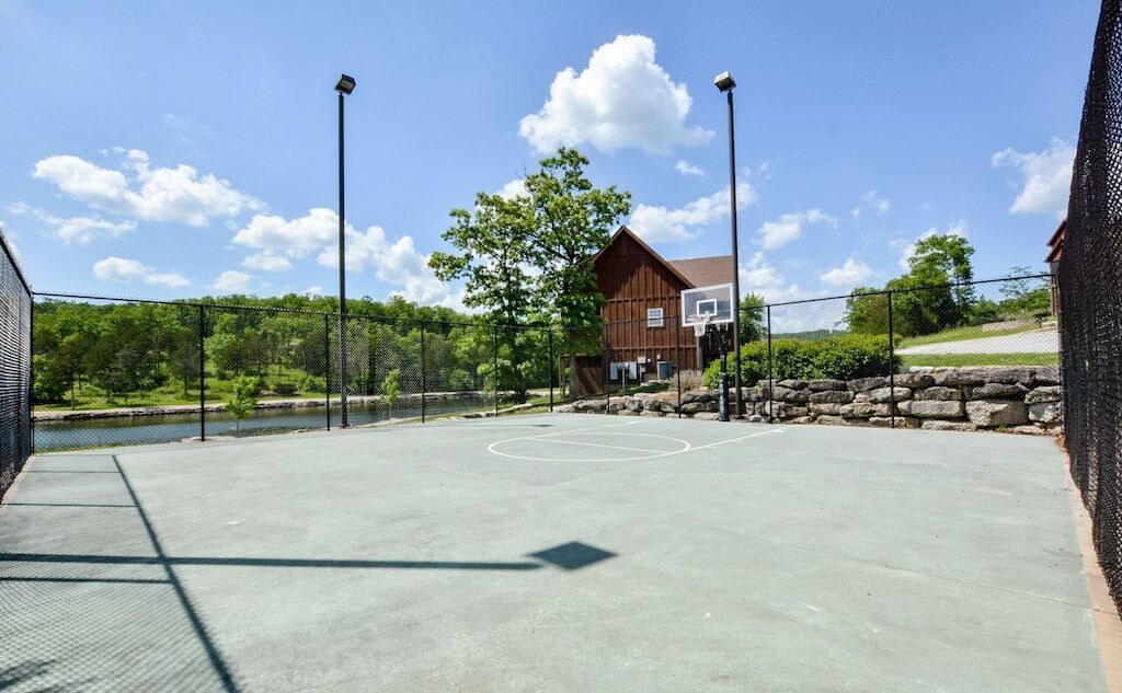 Ein Basketballplatz im Freien mit Netz, umgeben von einem Zaun, und ein Gebäude im Hintergrund.