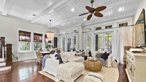 A spacious living room with a white sofa, a large ceiling fan, and a dining area with wicker chairs. - "116 Surfer Ln" | Resort Style Community Pool | Walk to Rosemary Beach (Seacrest Beach)