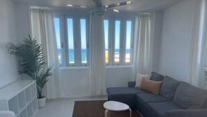 A modern living room with a grey sofa, a small round table, a potted plant, and a view of the sea through large windows. - Arecibo Hotel 4301 (Arecibo)