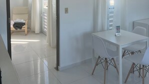 A bright, white room with a dining table and chairs, a chair with a blanket, and a view of the city through a window. - Arecibo Hotel 4301 (Arecibo)