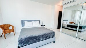 A modern bedroom with a bed, a chair, and a sliding glass door leading to another room. - Arecibo Hotel 3202 (Arecibo)