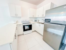 A modern kitchen with white cabinets, a stainless steel refrigerator, a microwave, and an oven.