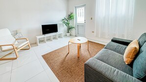 A modern living room with a sofa, a TV on a stand, a coffee table, and a potted plant. - Arecibo Hotel 3202 (Arecibo)