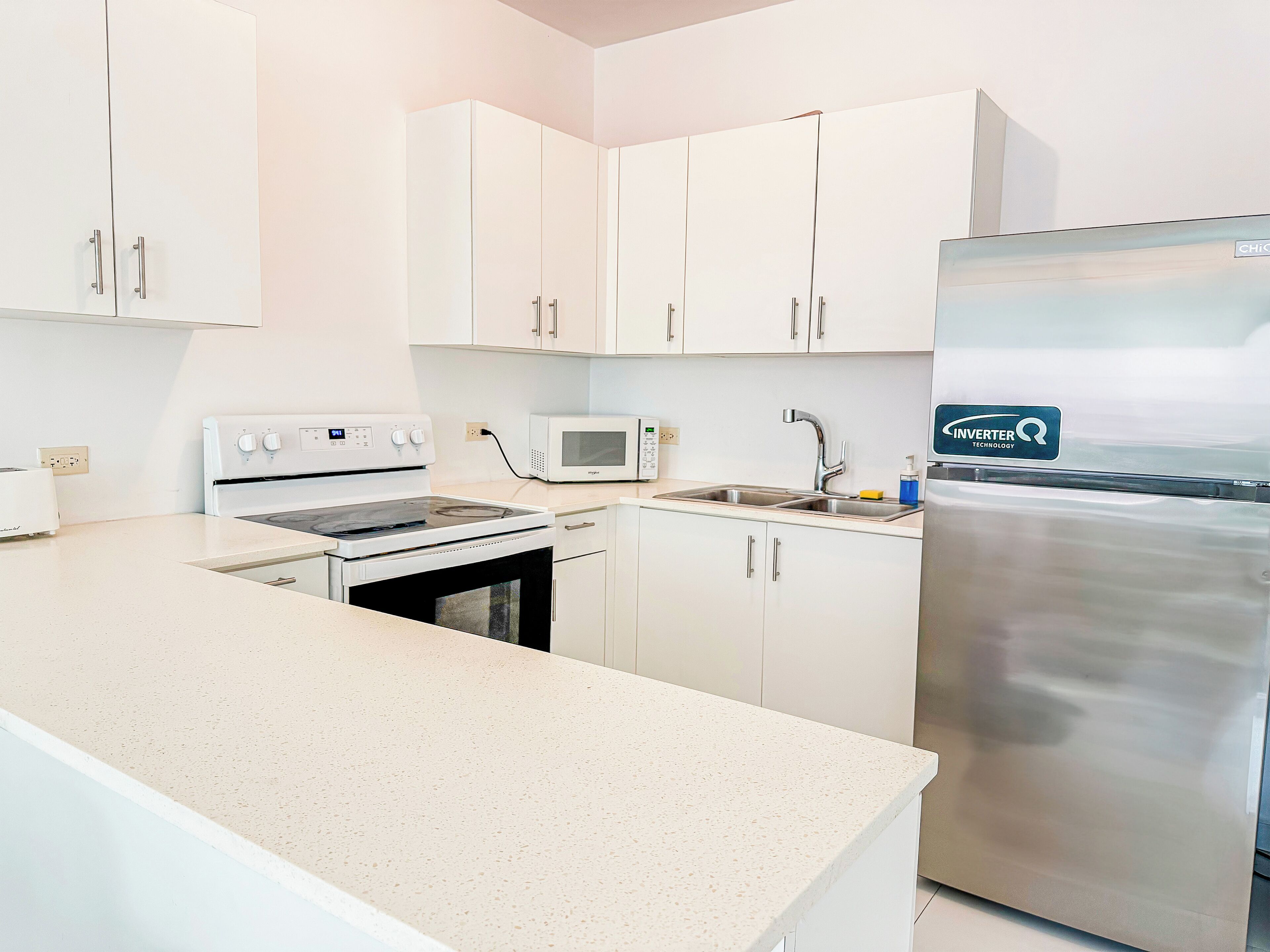 Une cuisine moderne avec des meubles blancs, un réfrigérateur en acier inoxydable, un four à micro-ondes et une cuisinière.