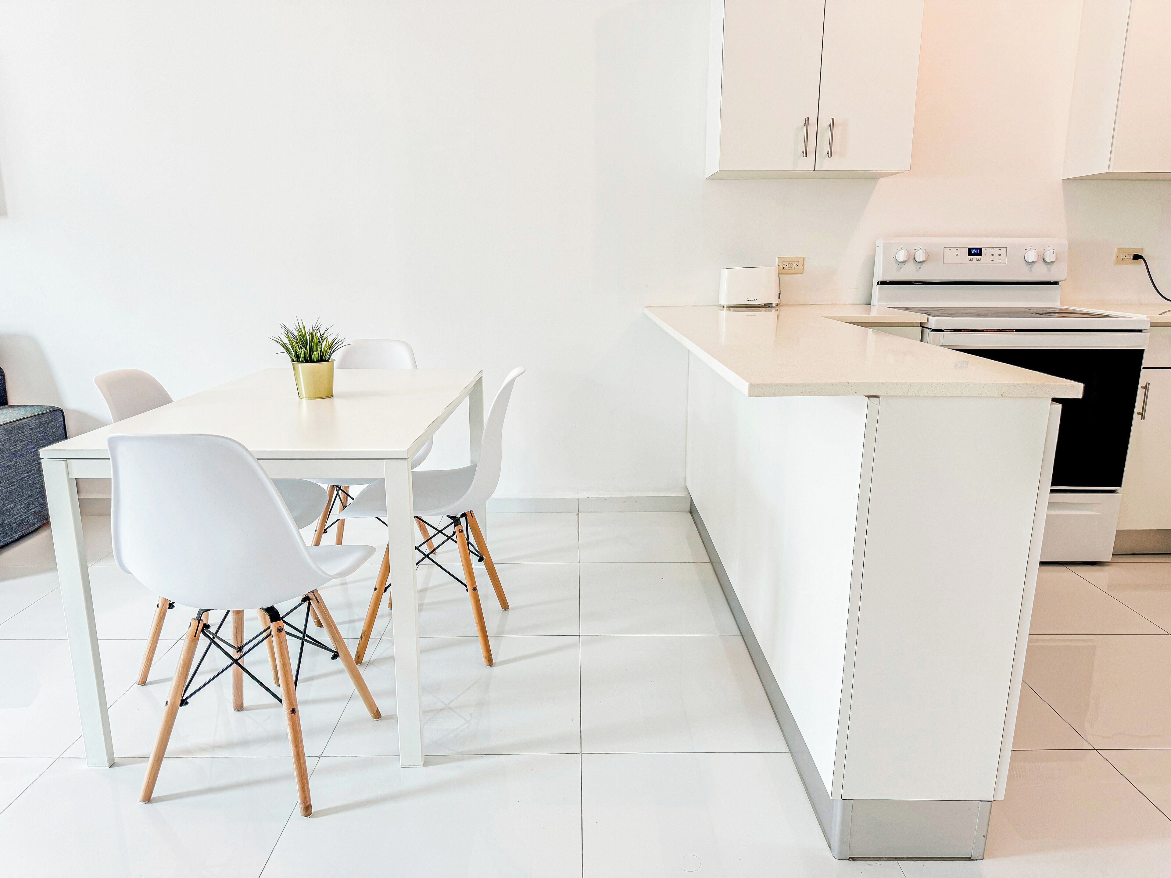 Une cuisine moderne avec des meubles blancs, un four encastré et un coin repas comprenant des chaises et une table, le tout dans des tons blancs.