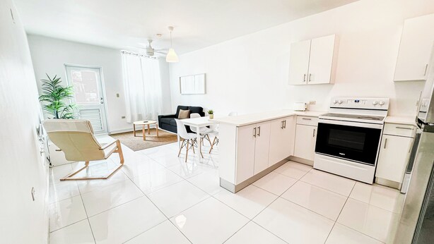 A modern kitchen with white cabinets, a built-in oven, and a dining area with a table and chairs. - Arecibo Hotel 3202 (Arecibo)