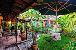 Un patio al aire libre con una pérgola de madera, plantas en macetas, un banco de piedra y una hamaca.