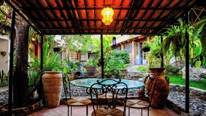 An outdoor patio with a round table and four chairs, surrounded by large planters and a rustic ceiling. - Casa Aurora Garden Retreat (Ajijic)