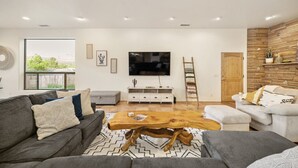 A modern living room with a large wooden coffee table, grey sofas, a white entertainment unit, and a TV mounted on the wall.