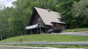 A rustic lodge with a steeply pitched roof, a large porch, and a sign indicating a leasing office.