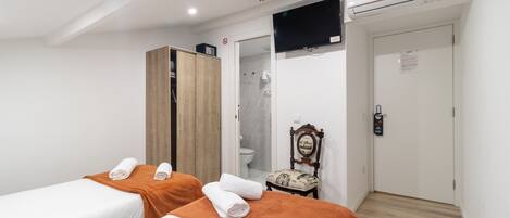 A hotel room with two beds, a wooden wardrobe, a television, an air conditioning unit, a bathroom with a shower, and a door with a sign.