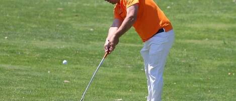 A person in an orange shirt and white pants playing golf.