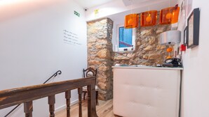 A staircase with a wooden handrail leading to a room with a stone wall, a white upholstered chair, and a small table with a lamp. - Coimbra City Charm (Coimbra)