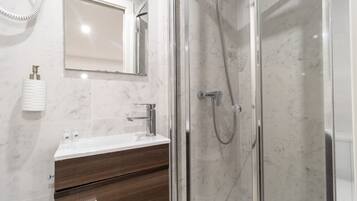 Un baño moderno con ducha de vidrio, lavabo blanco y tocador de madera.