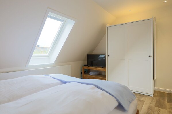 A bedroom with a bed, a TV on a wooden shelf, a wardrobe, and a skylight. - Friesland, Germany (Sylt)