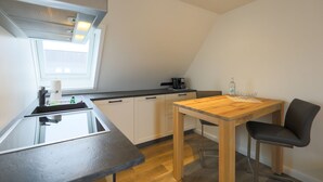 A compact kitchen with a wooden table and a chair, a window, and a modern stove.