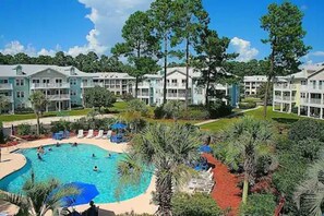 A resort with multiple-story buildings, a central swimming pool, and surrounding palm trees.