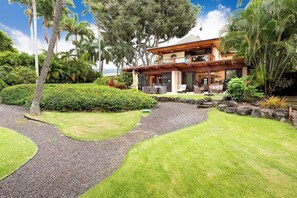 A modern two-story house with a landscaped garden, a pool, and a view of the ocean.