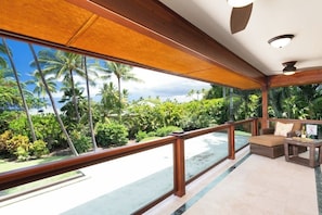 A balcony with a view of palm trees and a beach, furnished with a sofa and a table.