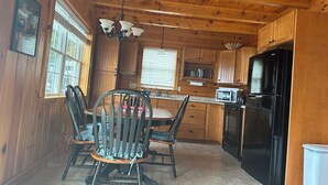 A wooden cabin interior with a dining area, kitchen, and a black refrigerator.