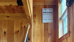 A wooden staircase with a handrail, a family rules sign, and a framed picture on the wall.