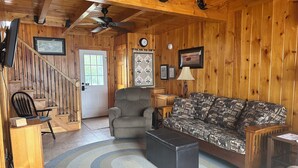 A wooden interior with a staircase, a sofa, a chair, a table, and a ceiling fan.