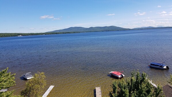 A lake with boats docked at the shore, surrounded by trees and hills in the background. - Ossipee Lake Water Front Property (Ossipee)