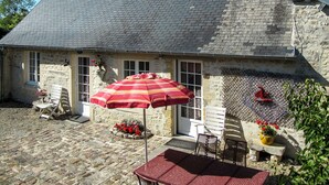 Ein Steinhaus mit Ziegeldach, einer Terrasse mit rotem Sonnenschirm und Sitzgelegenheiten im Freien.