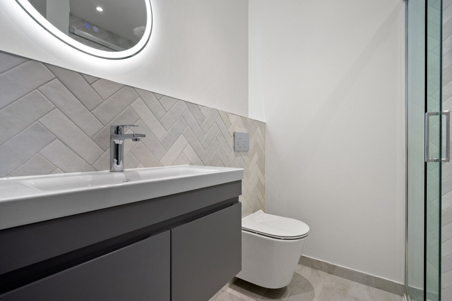 A modern bathroom with a herringbone tile backsplash, a white sink, and a toilet.