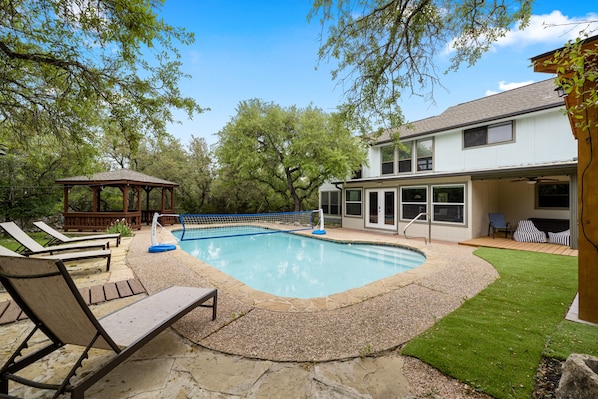 Ein Garten mit Swimmingpool, Liegestühlen, einem Pavillon und einem Haus mit überdachter Terrasse.