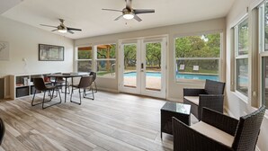 Eine großzügige Terrasse mit Essbereich, Korbmöbeln, Deckenventilatoren und Blick auf einen Swimmingpool.