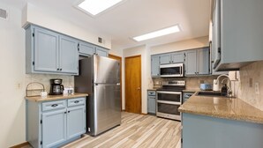 Eine Küche mit hellblauen Schränken, einem Edelstahl-Kühlschrank, einer Mikrowelle, einem Backofen und einer Kaffeemaschine.