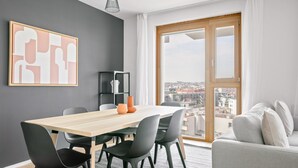 A modern living room with a dining area, a large window with a city view, and a grey accent wall. - Lovely Favoriten 3BR w/ Roof, Gym & Lounge, 1min to HBF, by Blueground (Vienna)